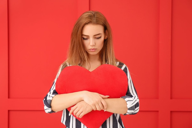 ragazza triste con cuscino a forma di cuore in mano