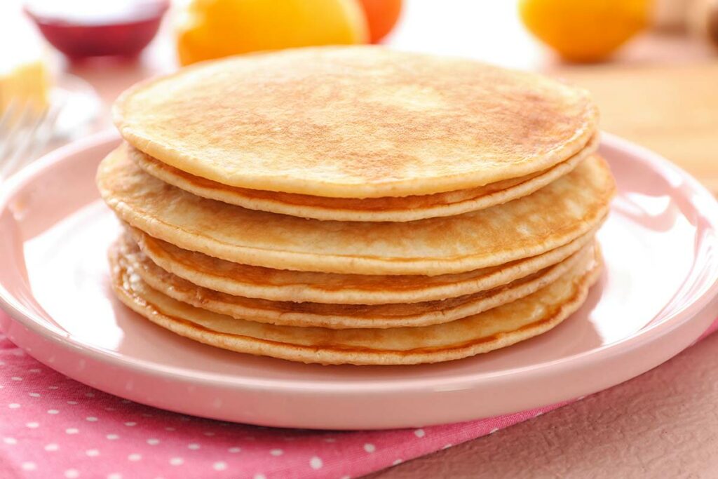 Piatto rosa con sopra una pila di pancake per colazione realizzati con ricetta Dukan