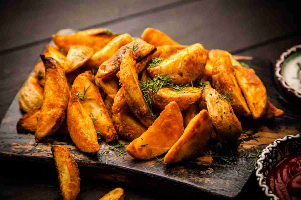 Contorni con le patate, spicchi al forno su un vassoio di ardesia