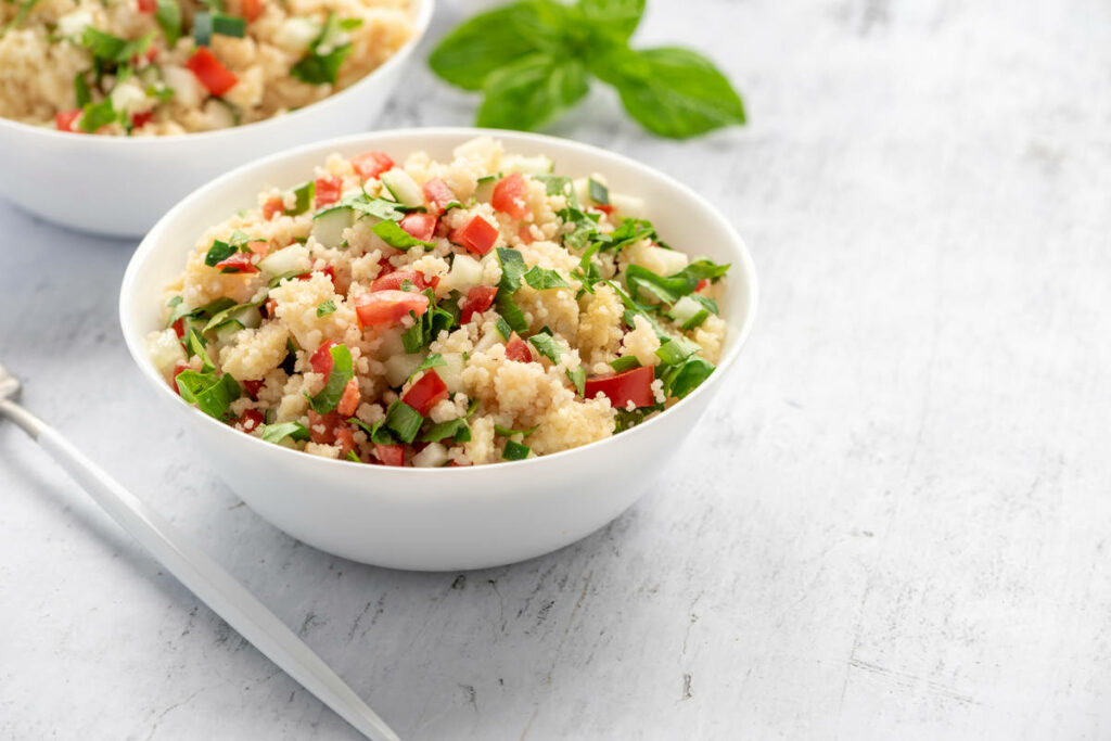 cous cous con pomodori, cetrioli, prezzemolo, in una ciotola bianca sul tavolo.