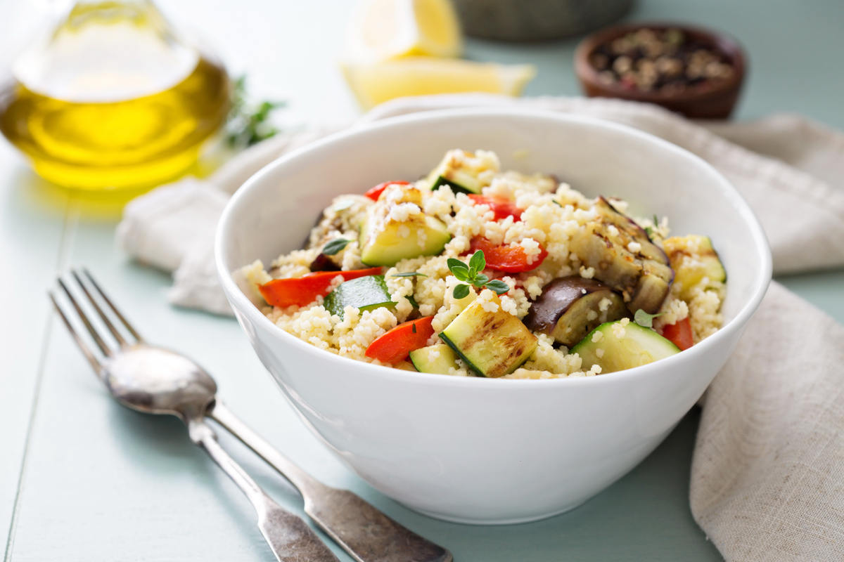 piatto di couscous con zucchine, peperoni e melanzane grigliate su tavolo con posate e olio nello sfondo