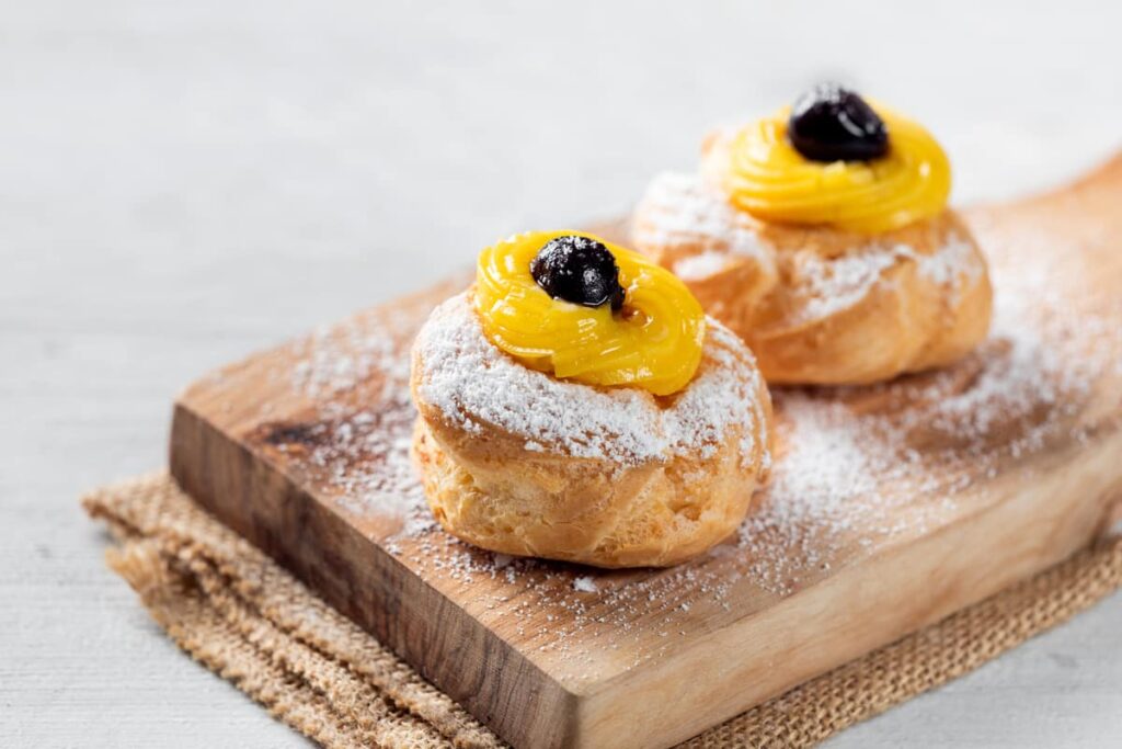 tagliere con due zeppole napoletane fritte con zucchero a velo crema e amarena