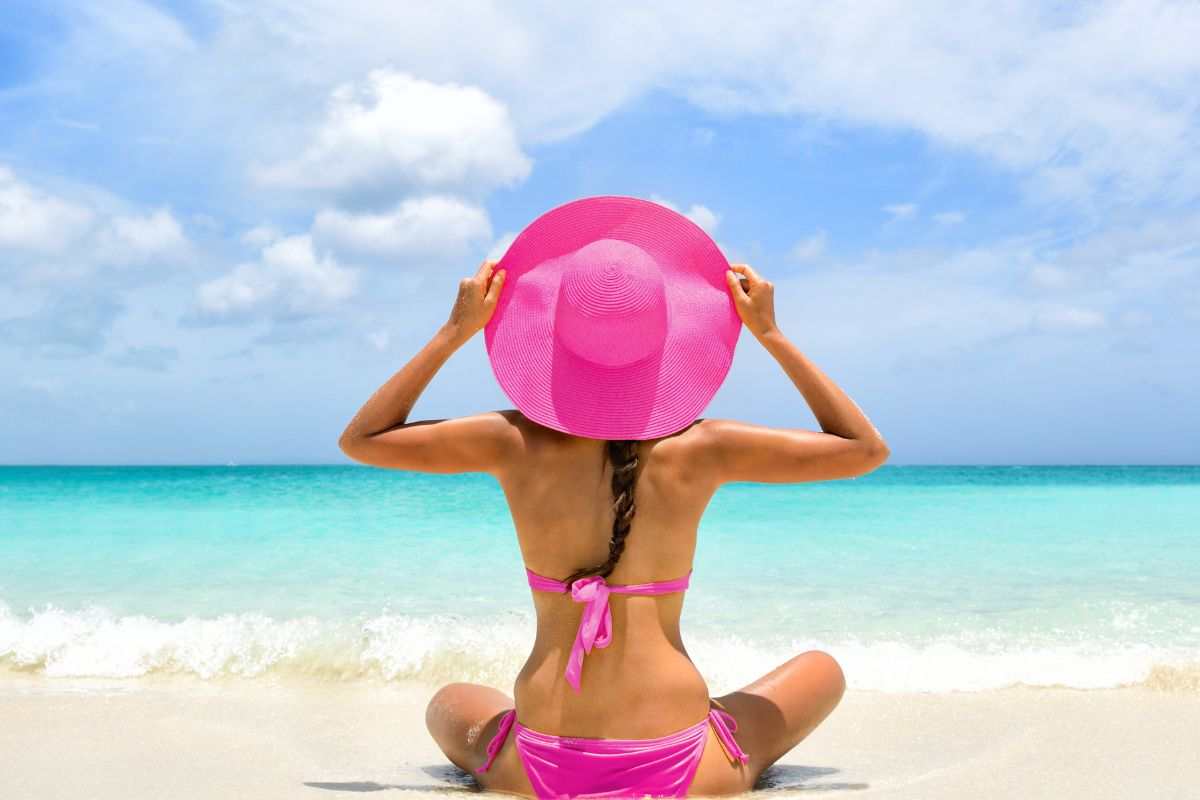 ragazza al mare di spalle con costume rosa e cappello