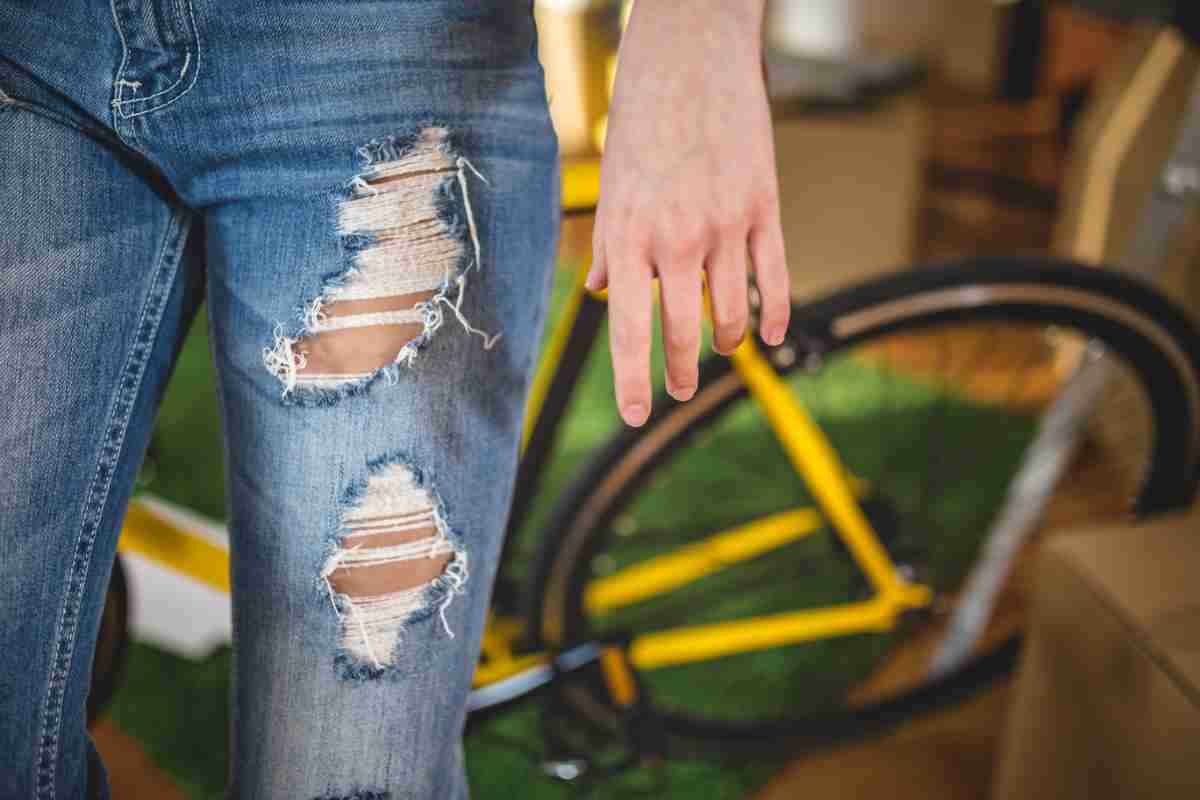 Ragazza che indossa dei jeans strappati con una bici gialla sullo sfondo