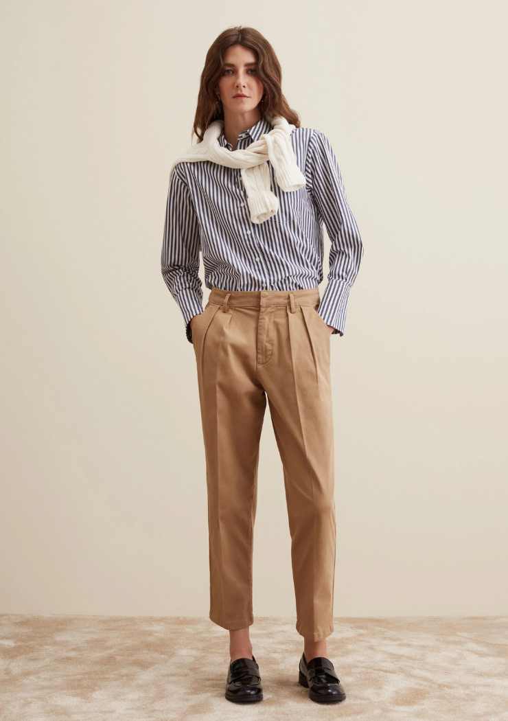 modella con pantaloni chino, camicia a righe e pullover sulle spalle