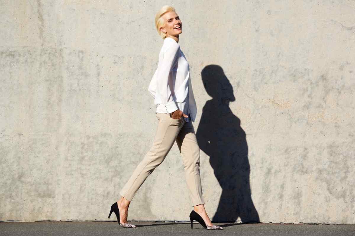 donna che cammina con pantaloni beige, camicia bianca e décolleté