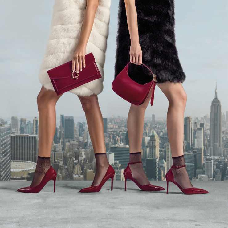 gambe modelle con scarpe eleganti con tacco alto rosso ciliegia, clutch e borsa a mano