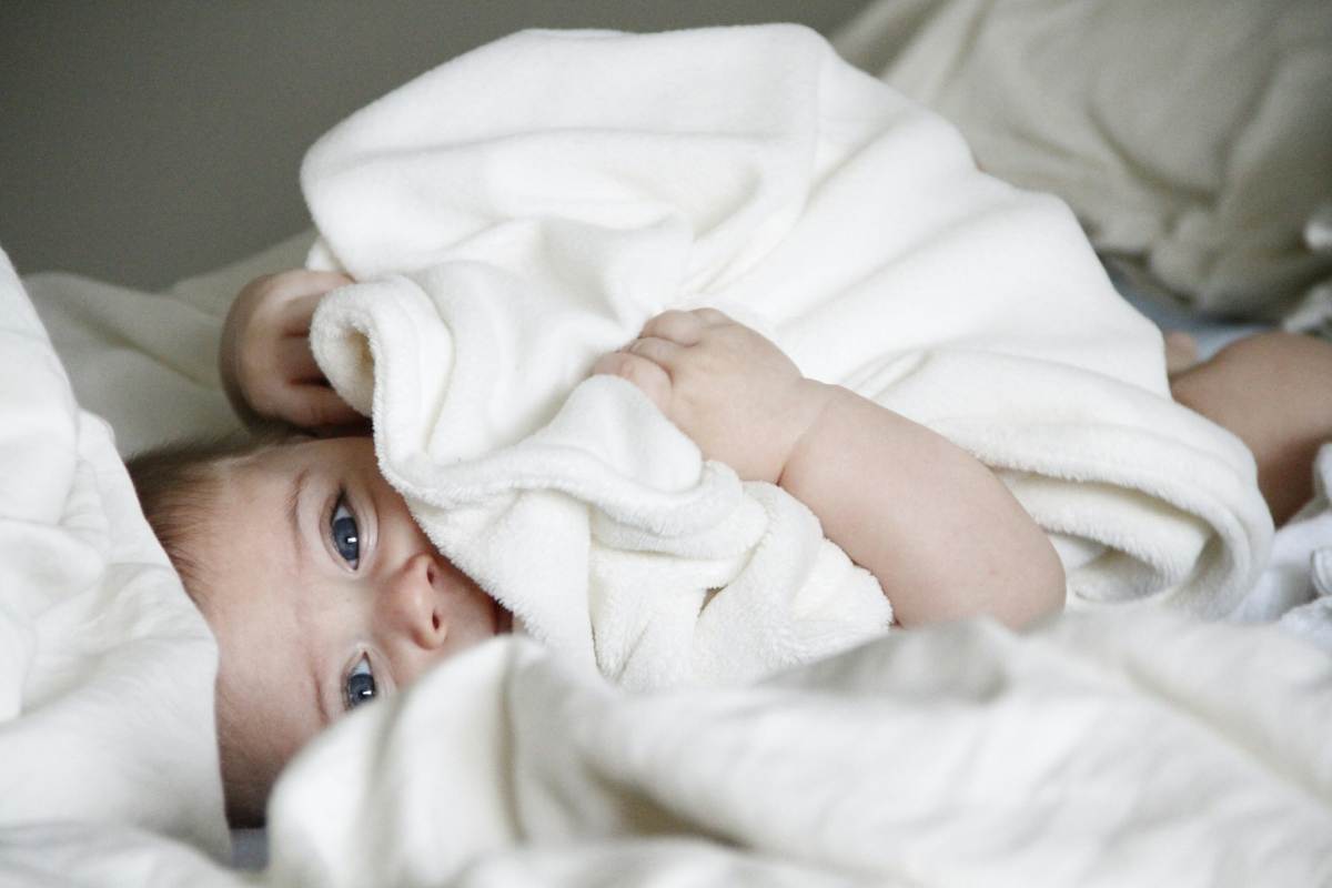 Un bambino con addosso delle coperte del suo corredo