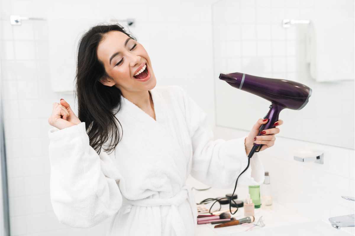 donna sorridente che asciuga i capelli in bagno