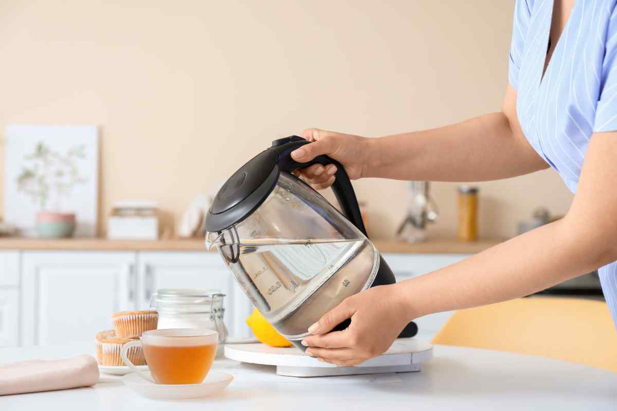 dettaglio donna che versa acqua da un bollitore elettrico in cucina