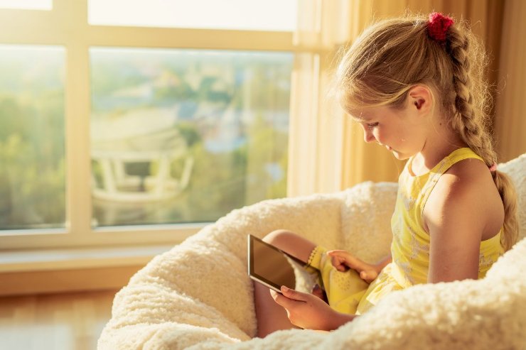 bambina seduta su una poltrona con in mano un tablet