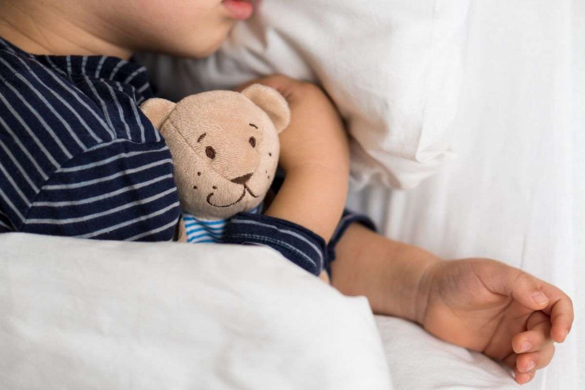 bambino sdraiato a letto sotto le lenzuola con il suo peluche