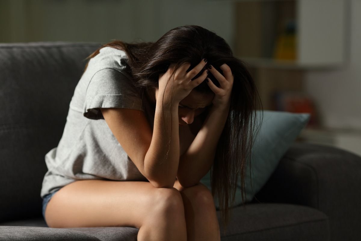 ragazza seduta sul divano con le mani tra i capelli