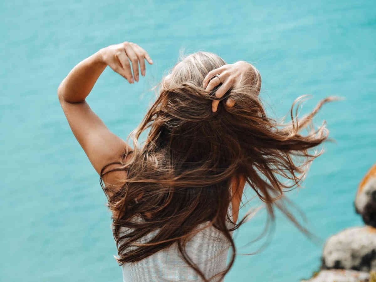 Ragazza con i capelli lunghi sciolti, di spalle davanti al mare